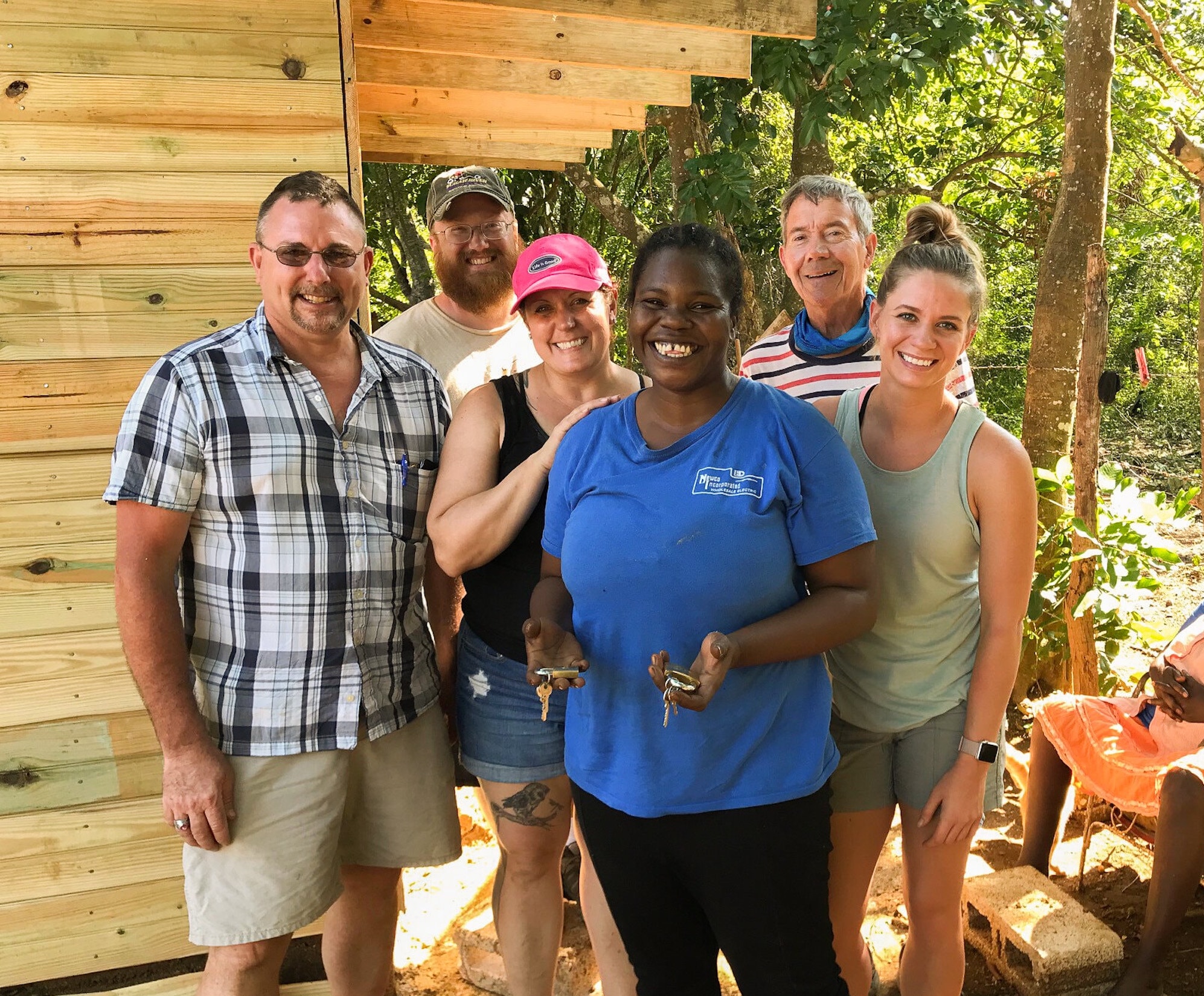 Group of volunteers smiling in front of a wooden house under construction.